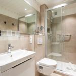 Badezimmer mit Dusche, Waschbecken und Toilette. Wandfliesen und Spiegel sichtbar.