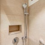 Dusche mit Handbrause und eingelassenem Regal an hellen Fliesenwänden.
