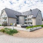 Modern multi-family house with balconies and paved forecourt.