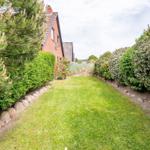 Garten mit Rasenfläche, Beete und Hecken entlang eines Hauses.