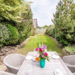 Garten mit Tisch, Stühlen und Blumenarrangement zwischen Hecken und Bäumen.