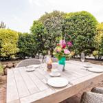 Garten-Tisch mit Platz für vier Personen, Blumen und Weinflasche.