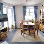 Dining room with wooden table, chairs, and cabinet. TV, curtains, and rug visible.