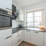 Kitchen with white cabinets, stainless steel oven, and window with curtains.