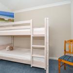 A bedroom with bunk bed, chair, and wall picture