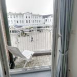Balcony with white lounge chair and view of busy square with shops and pedestrians.