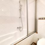 Bath with shower, toilet, and tiled wall with mosaic strip.