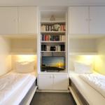 Zwei Einzelbetten mit Nachttischen und integriertem TV-Bereich mit Bücherregal.
