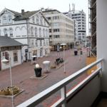 Blick von Balkon auf belebte Straße mit Geschäften und Parkplätzen.