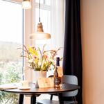 Runder Tisch mit Blumen, Flasche und Tasse vor Fenster mit Blick auf Garten.