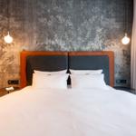 Ein Bett mit weißer Bettwäsche, einem grauen Kopfteil und orangefarbenen Akzenten an der Wand.