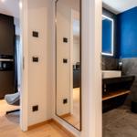 Badezimmer mit blauer Wand und Waschtisch. Küche mit dunklen Schränken sichtbar.