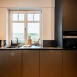 Moderne Küche mit Fenster, Spüle, Dunstabzug und integriertem Ofen.