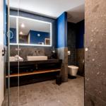 Badezimmer mit Dusche, Waschbecken und Toilette. Dunkle Fliesen und blauer Akzent.