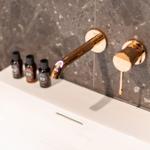 Waschbecken mit goldenem Wasserhahn und drei Fläschchen auf der Oberfläche.