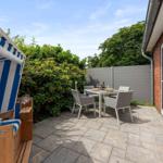 Terrace with beach chair, table and chairs. Backyard with hedge and house wall.