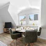 Dining room with round table, four chairs, and two windows. Wooden floor and TV corner.