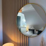 Round mirror with gold frame on wall with wooden verticals.