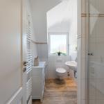Bathroom with shower, sink, and toilet. Wooden floor and white tile flooring.