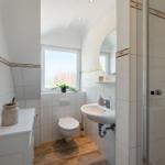 Bathroom with shower, sink, and toilet. Wooden floor and window with plant.