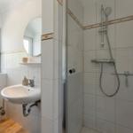 Bathroom with shower, sink, and toilet. Window with plant.