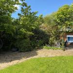 Garden with stone paving, grass area, hanging chair, and beach chair under trees.