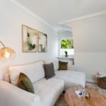 Living room with sofa, table, and window. Wall art and floor lamp visible.