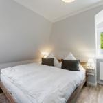 Bedroom with double bed, two windows, and wooden floor.
