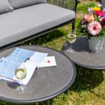 Zwei runde Tische mit Wein, Blumen und Broschüren im Garten.