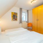 Schlafzimmer mit Doppelbett, Holzschrank und Fenster mit Vorhängen.