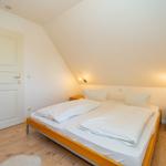 Schlafzimmer mit Doppelbett, Holzboden und Nachttischen an der Wand.