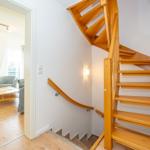 Holzgetreppe führt zur Wohnung. Im Hintergrund ist Wohnzimmer mit Sofa und Fernseher.