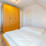 Schlafzimmer mit Bett, Kleiderschrank und Stuhl. Dachschrägen-Decke und Holzboden.