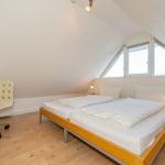 Schlafzimmer mit Doppelbett, Schreibtisch und Fenster unter Dachschrägen.