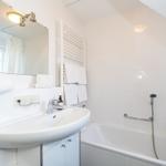 Badezimmer mit Badewanne, Waschbecken und Spiegel. Weiße Fliesen und Handtücher.