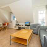 Wohn- und Essbereich mit Sofa, Couchtisch und TV. Holzboden und große Fenster.