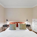 Schlafzimmer mit Bett, Nachttischen und Kleiderschrank. Fenster mit Rollladen und dekorativen Kissen.