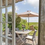 Durch die Glastür blickt man auf eine Terrasse mit Tisch, Stühlen und Sonnenschirm.