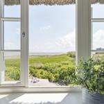 Durch das Fenster blickt man auf eine grüne Landschaft und das Meer.