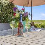 Terrasse mit Tisch, Stühlen, Blumen und Flasche Rosé unter Sonnenschutz.