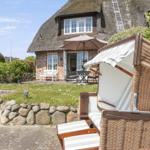 Haus mit Strohdach, Gartenbereich mit Liegestuhl und Terrasse mit Tisch und Stühlen.