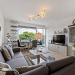 Living room with sofa, TV, and dining area. View to balcony with garden.
