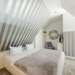 Bedroom with sloped ceiling, striped wall, and white bed.