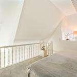 Bedroom with sloped ceiling, bed, window, and white balustrade.