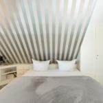 Bedroom with striped wall, white bed, and nightstand.