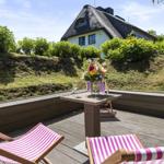 Terrace with loungers and table. House with thatched roof in background.