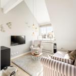 Living room with sofa, armchair, TV, and window. Shelf with glasses and decor.