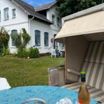 Haus mit Garten, Sonnenschirm und Tisch mit Flasche.
