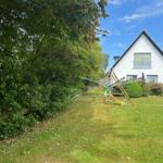 Ein weißes Haus mit Garten, Spielplatz und Blumen. Hinterhof mit Bäumen und einem Wäscheständer.