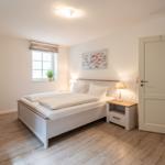 Schlafzimmer mit Bett, Nachttisch, Fenster und Tür.